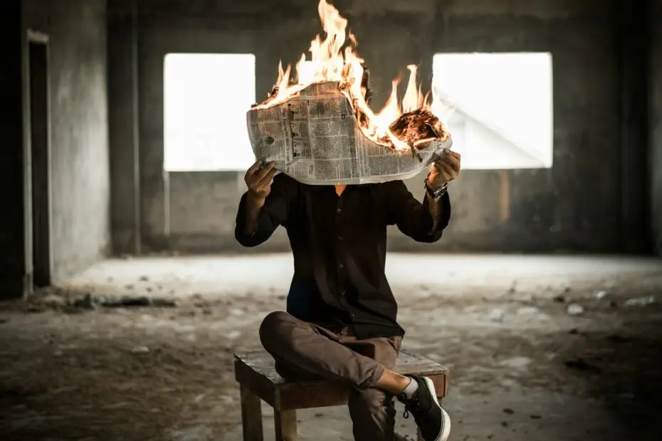 man sitting on chair holding newspaper on fire